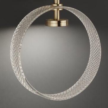 Contemporary Glass Wall Light A close-up of the Contemporary Glass Wall Light showcases a sculptural, textured glass ring elegantly suspended from a brass mount against a dark gray background. The illumination casts a portion of the ring in light, creating delicate shadow effects.