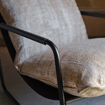 Close-up of the Contemporary Mid Century Style Metal Armchair, showcasing its cushioned backrest and seat upholstered in a textured, light beige fabric. The chair features black metal armrests and a sleek, minimalist design that enhances its modern aesthetic.
