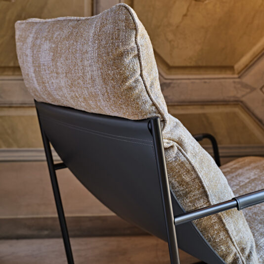 Contemporary Mid Century Style Metal Armchair The image showcases the Contemporary Mid Century Style Metal Armchair, highlighted with a close-up view of its sleek metallic frame. The chair is adorned with a plush, light brown, textured fabric cushion, set against a subdued, minimalist backdrop.