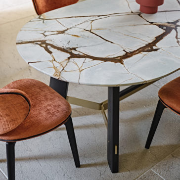Contemporary Oval Quartz Dining Set The Contemporary Oval Quartz Dining Set boasts a round marble table with striking gold and brown veining, set against a textured grey floor. Accompanied by sophisticated orange upholstered chairs with wooden legs, one of which is partially tucked under the table, a small decorative item enhances its appeal.