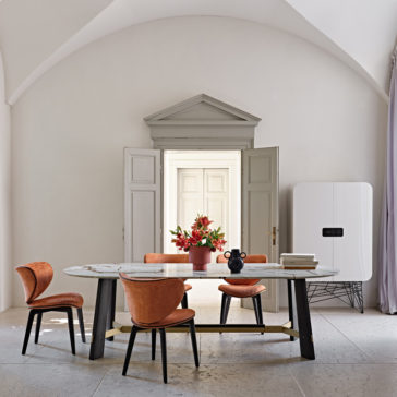 Contemporary Oval Quartz Dining Set A contemporary dining room showcases the elegant Contemporary Oval Quartz Dining Set, complete with four orange upholstered chairs. The table is adorned with a bouquet of red flowers in a vase, a small black sculpture, and several stacked books. The room features arched ceilings, a doorway, and a minimalist white cabinet.