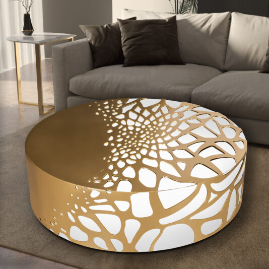 Modern living room showcasing the Exclusive Cut Out Round Coffee Table in a metallic gold finish, characterized by its intricate geometric design. The table is positioned in front of a plush gray sectional sofa decorated with an assortment of gray and brown cushions.