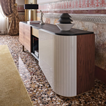 A High End Modern Canaletto Walnut Sideboard with glossy white surfaces stands against an ornate wall adorned with intricate red and gold designs. The stylish sideboard is decorated with a small statue, a black lamp, and stacked bowls. The floor features a terrazzo pattern.
