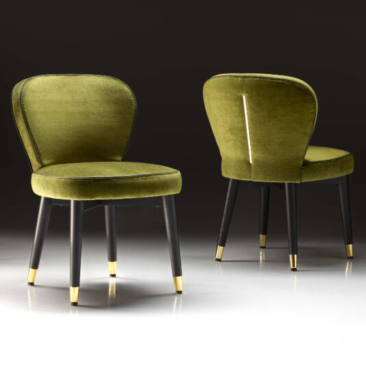 The luxurious High End Velvet Dining Chairs feature green upholstery and dark wooden legs adorned with gold tips. The image showcases one chair facing forward and the other backward against a dark backdrop, emphasizing their elegant design and plush texture.