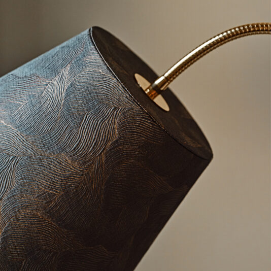 Large Modern Studio Style Floor Lamp Close-up of a textured cylindrical lampshade with intricate patterns, held by a flexible, gold-colored gooseneck arm. The background is blurred and neutral, highlighting the details of this Large Modern Studio Style Floor Lamp.