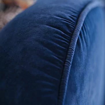 Large Modern Velvet Modular Sofa Close-up of a plush blue fabric surface from the Large Modern Velvet Modular Sofa, highlighting its soft texture and intricate stitching along the seam. The fabric appears smooth and velvety, gently reflecting light. The background is blurred, emphasizing the detail of the blue material.