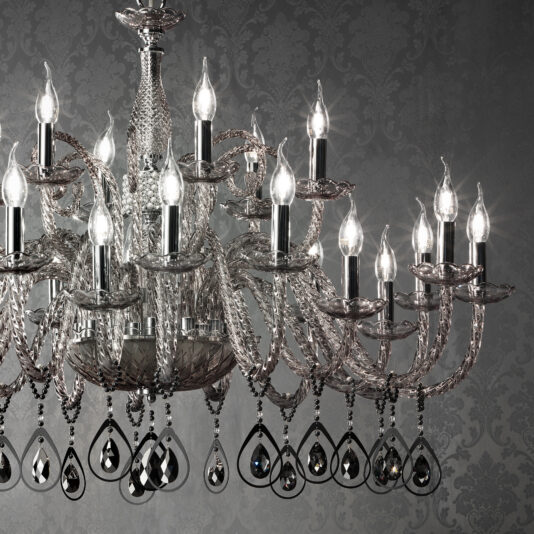 A large Smoked Glass Chandelier With Pendant Drops is hanging against a textured grey background. The chandelier features intricate designs with clear and dark crystal ornaments, including pendant drops, dangling from its arms. The background has an ornate, elegant pattern.