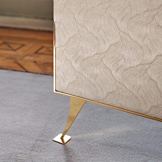 Luxury 3 Leaf Dressing Screen Close-up of a luxury piece of modern furniture with an ornate, textured beige surface and gold metallic legs, placed on a light-colored carpet. Nearby, the Luxury 3 Leaf Dressing Screen adds elegance to the scene. The floor in the background has a patterned hardwood finish.