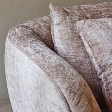 Luxury Contemporary Sofa Close-up shot of the Luxury Contemporary Sofa highlighting its armrest and two cushions. The beige, textured fabric looks soft and slightly worn, imparting a cozy and inviting ambiance to this modern piece of furniture. The background features a neutral gray wall.