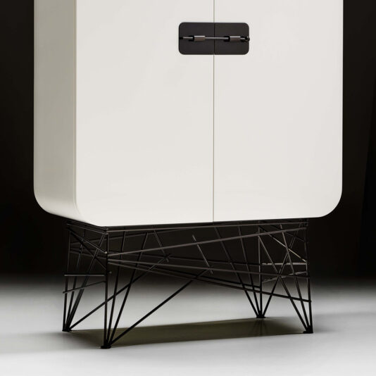 Modern Lacquered Cabinet The Modern Lacquered Cabinet features a minimalist white design with black geometric metal legs and handles. It boasts smooth, rounded corners and a sleek, modern aesthetic, complemented by intricate angular base supports set against a dark background.