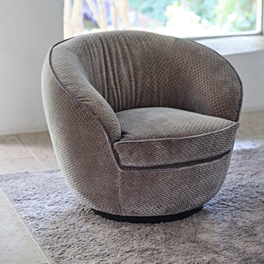 A **Modern Luxury Swivel Armchair** with a textured fabric surface is placed on a light gray rug. The chair is positioned near a large window that lets in natural light, and the background features a neutral-toned floor and a blurred outdoor view.