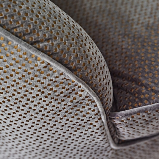 Close-up of the Modern Luxury Swivel Armchair, upholstered in grey fabric adorned with a small, uniform pattern of golden dots. The image captures the chair's seam and contours, emphasizing the texture and intricate detail of the upholstery.