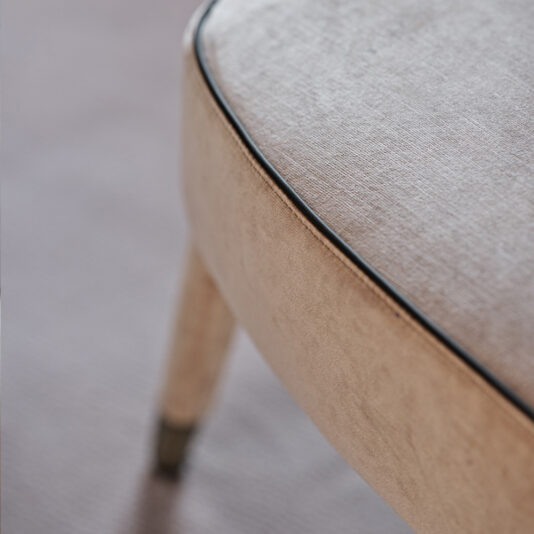 Close-up of a beige upholstered Modern Velvet Occasional Armchair, featuring a black-edged seam. The chair's wooden legs are slightly visible. The focus is on the texture and fabric detail of the seat and back, with soft lighting creating a serene atmosphere.