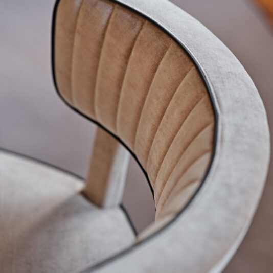 Close-up of the backrest of the Modern Velvet Occasional Armchair in beige upholstery, featuring vertical stitching detail and black piping along the edges. The image brings attention to the curvature and texture of the chair's fabric, showcasing its elegant and contemporary design against a blurred background.