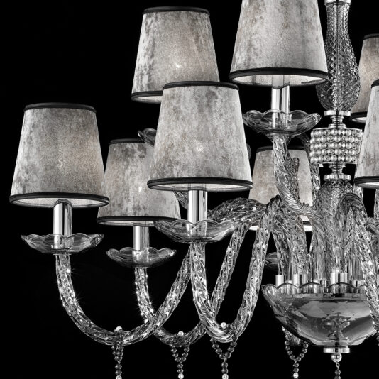 A close-up of the Smoked Glass Chandelier With Shades, showcasing its multiple intricately designed crystal arms. Each arm supports a lamp adorned with a soft, silver-gray shade. The chandelier and lamps are set against a black background, accentuating their luxurious appearance.