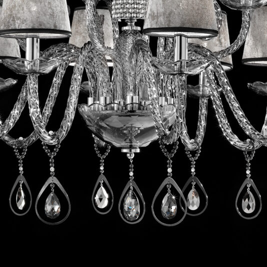 A close-up of the Smoked Glass Chandelier With Shades reveals its elegance through multiple arms adorned with hanging crystal teardrop ornaments. This chandelier, featuring metal accents and several shaded lights, creates a sophisticated and opulent appearance against a black background.