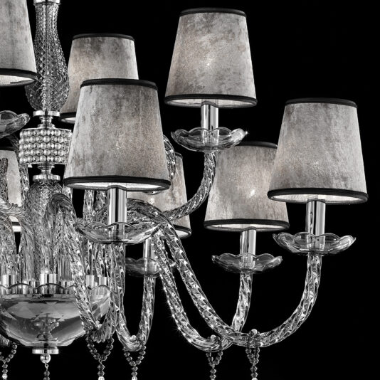 A close-up shot of the elegant Smoked Glass Chandelier With Shades showcases its multiple arms and textured grayish lampshades. The chandelier features intricate glasswork adorned with crystal accents, all beautifully highlighted against a black background.