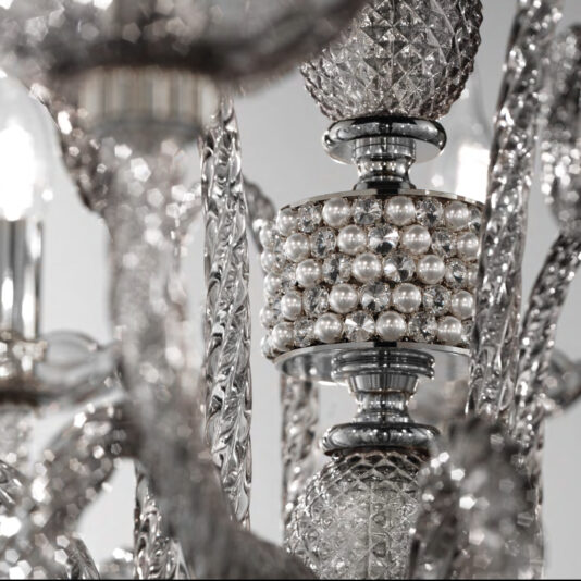 Close-up of the Large Smoked Glass Chandelier With Pendant Drops, featuring intricately crafted crystal and metal parts, adorned with a cylindrical segment that has small pearl-like beads. The background softly blurs out, putting focus on the elaborate design details.