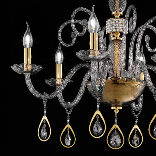 A close-up view of the Smoked Glass Chandelier With Swarovski® Crystals And Pearls showcases its elegant smoked glass design and gold accents with intricate detailing. The chandelier features several lit candle-shaped bulbs, Swarovski® crystals, and pearls hanging from its curled arms, all set against a black background.