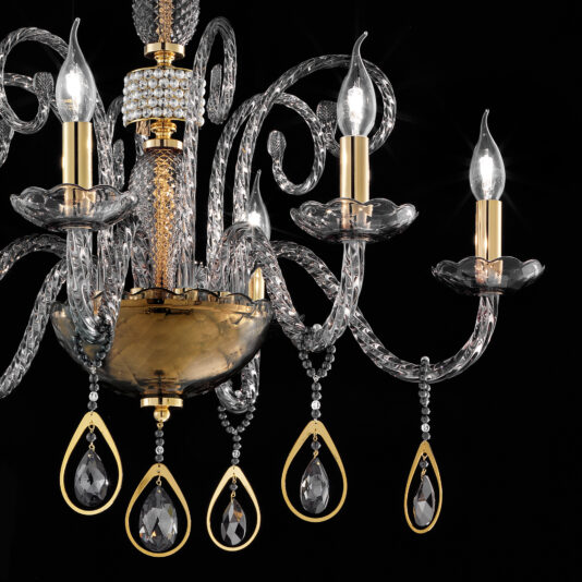 A close-up of the Smoked Glass Chandelier With Swarovski® Crystals And Pearls against a black background. This ornate chandelier showcases intricate glass arms, candle-shaped bulbs, and hanging crystal pendants, all complemented by golden accents that add a touch of elegance to its detailed craftsmanship.