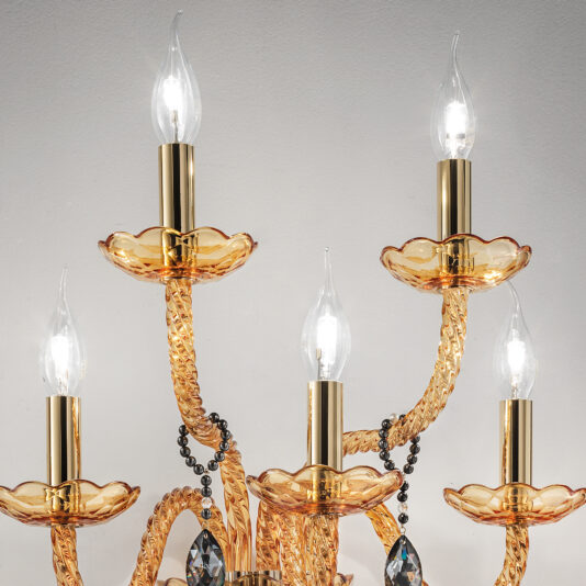 Amber Glass 5 Arm Wall Light A detailed image of an elegant chandelier featuring multiple twisting amber glass arms with a gold tint. Each arm, similar to those on the Amber Glass 5 Arm Wall Light, holds a candle-shaped bulb surrounded by gold fluted holders. Black crystal beads and faceted teardrop crystals dangle from the structure, adding a touch of luxury.