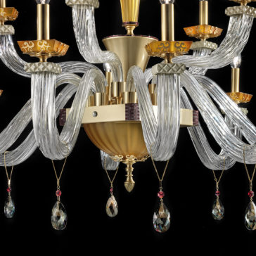 Introducing the Elegant Amber Glass Chandelier: a luxurious lighting fixture crafted from amber glass and featuring a stunning gold and brass centerpiece. Adorned with gracefully curved glass arms, this chandelier boasts candle-like light fixtures and is beautifully accented with hanging crystal pendants, each highlighted by a subtle red hue, set against an exquisite black backdrop.