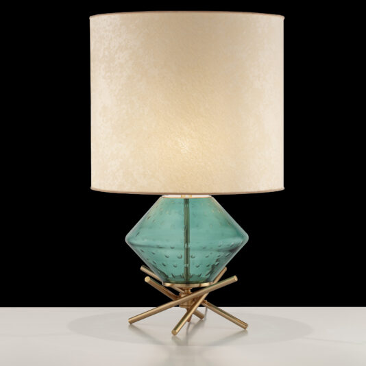 The Hand Blown Glass Table Lamp features a modern design with a cylindrical beige lampshade atop a blue-green diamond-patterned glass base. The base is supported by a geometric, gold-colored metal stand and is showcased on a white surface against a black background.