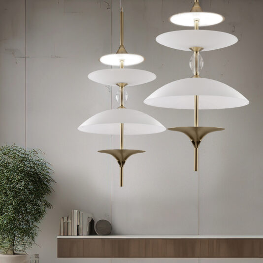 Modern interior featuring three contemporary pendant lights, including the Large Modern Venetian Glass Pendant Light with white and brass finishes, hanging at different heights against a minimalist gray wall. A wooden shelf below holds a small arrangement of books, and a lush green potted plant adds a touch of nature.
