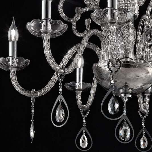 A close-up image of the Smoked Glass Chandelier With Pendant Drops, showcasing its intricate, curved arms and teardrop-shaped pendant accents. The chandelier features lit candle-shaped bulbs that stand out against a dark background, emphasizing its elaborate design and sparkle.

