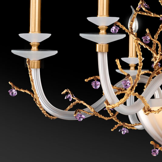 A close-up of the Candle Style Chandelier With Swarovski Crystal Flowers showcases its gold and white arms with candle-like lights. Delicate gold branches entwined with Swarovski crystal flowers and small purple gem-like ornaments add luxurious, intricate details to the design, all set against a black background.
