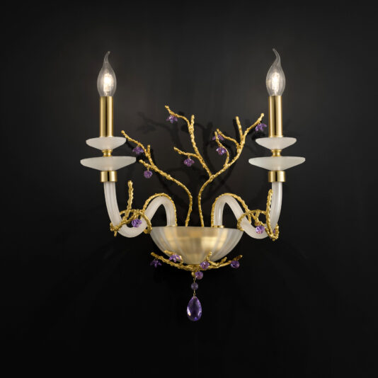 The Candle Style Wall Light With Swarovski Crystal Flowers features two upward-facing, candle-shaped lights on brass stems with purple and gold accents that resemble delicate branches. Adorned with Swarovski crystal flowers and a central bowl-like element, the sconce is mounted on a black background.