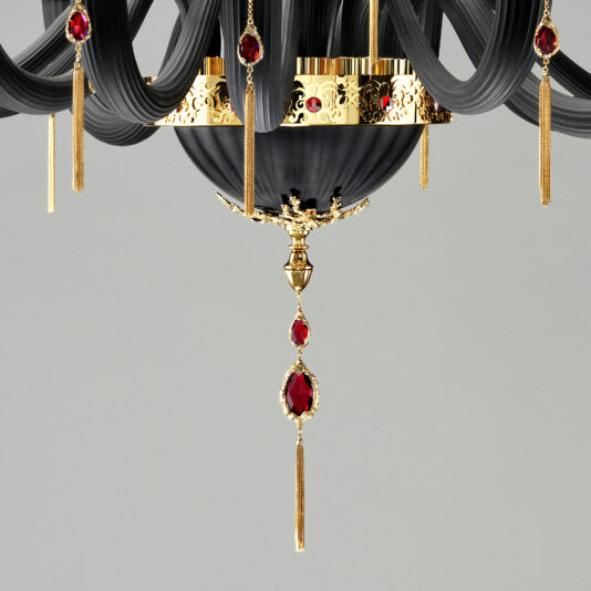 The Classic Black Chandelier With Swarovski® Crystals boasts sophisticated, curved black arms and luxurious gold accents adorned with red gemstones. Thin gold pendant details hang from various points, adding an extra touch of opulence. Set against a plain and neutral background, this chandelier is truly a timeless masterpiece.