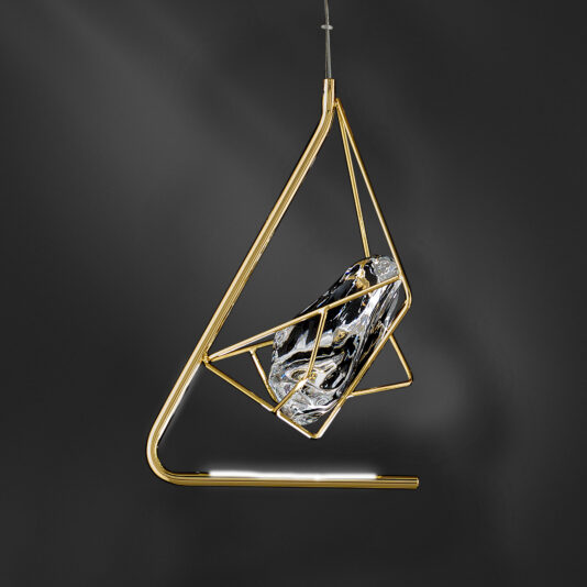 The Crystal Rock Pendant Light features a modern triangular gold frame that suspends an abstract, sculpted glass element. The glass showcases a marbled black, white, and gold texture, offering an artistic and contemporary design against a dark gray background.