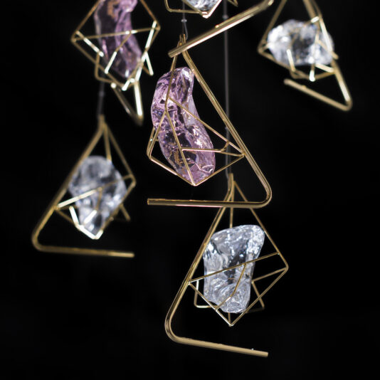 Crystal Rock Pendant Light Cluster A close-up view of the Crystal Rock Pendant Light Cluster showcasing large, semi-transparent gemstones in purple and clear tones, encased in delicate geometric wire frames. The artistic arrangement of the gemstones creates a striking visual against a dark background, reminiscent of hanging pendant lights.