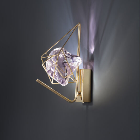 The Crystal Rock Wall Light boasts a modern gold-framed wall sconce with a sophisticated geometric design. At its heart lies a clear, irregularly shaped crystal rock that refracts light beautifully, creating dynamic shadows on nearby surfaces. Set against a smooth, dark background, it offers an exquisite lighting experience.