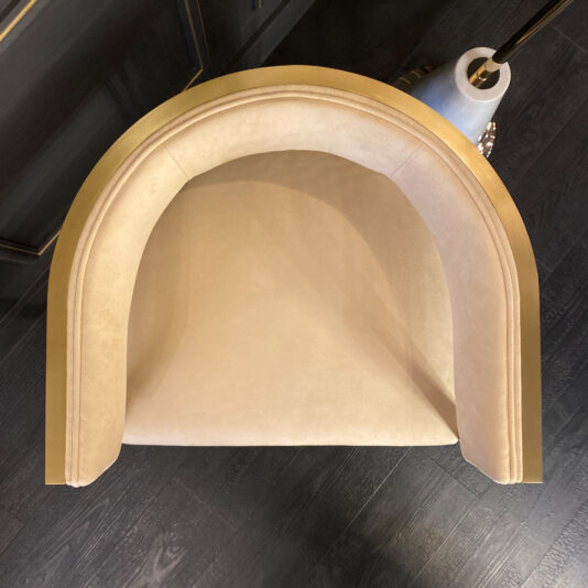A top-down view showcases the Exclusive Contemporary High End Dining Chair, featuring luxurious beige velvet and elegant curved golden edges. The chair is set against a dark wooden floor, while the corner of a white vase adorned with gold decoration adds to the contemporary elegance in the upper right corner.