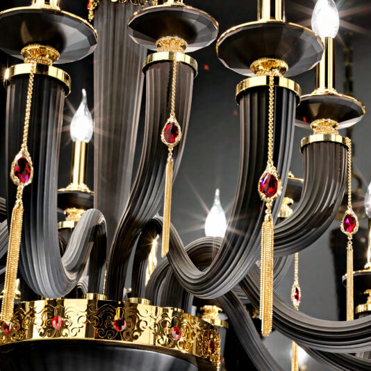 A close-up image of the Large Classic Black Chandelier With Swarovski® Crystals, featuring curved dark metal arms adorned with elegant gold details, tassels, and red Swarovski® crystals dangling from its structure. Numerous lit candle-shaped bulbs enhance its luxurious appearance.