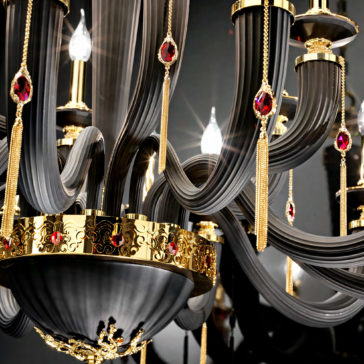 Large Classic Black Chandelier With Swarovski® Crystals The Large Classic Black Chandelier With Swarovski® Crystals is a luxurious piece adorned with ornate black curved arms, gold accents, and red gemstone-like decorations. This classic design features intricate detailing and multiple lit bulbs that create a sparkling and opulent appearance.