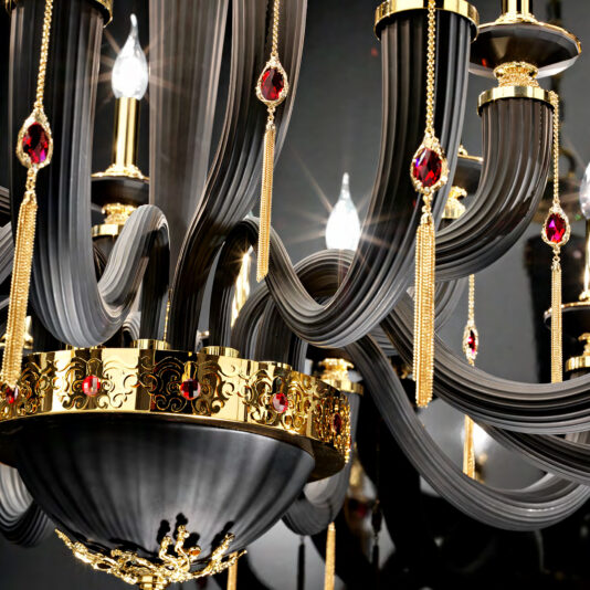 The Large Classic Black Chandelier With Swarovski® Crystals is a luxurious piece adorned with ornate black curved arms, gold accents, and red gemstone-like decorations. This classic design features intricate detailing and multiple lit bulbs that create a sparkling and opulent appearance.