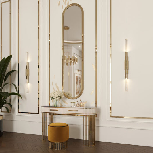 Large Lozenge Modern Wall Mirror A luxurious vanity setup featuring a Large Lozenge Modern Wall Mirror with gold accents on a cream-colored wall, accompanied by a sleek white and gold table, a mustard yellow cushioned stool, and elegant wall-mounted lights. A plant is seen on the left side.