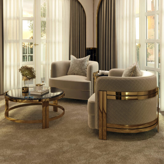 A sophisticated living room features two Modern Curved Armchairs With Brass Frames, a round gold and glass coffee table, a book, a vase with flowers, and two large windows draped with sheer and blackout curtains. The room is bathed in natural light.