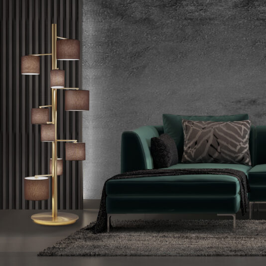 A modern living room features a dark teal sectional sofa adorned with patterned and solid pillows. Beside it stands the Modern Floor Lamp With Shades, showcasing its sleek design and multiple brown shades. The backdrop includes a textured gray wall, with a plush gray rug beneath the furniture.