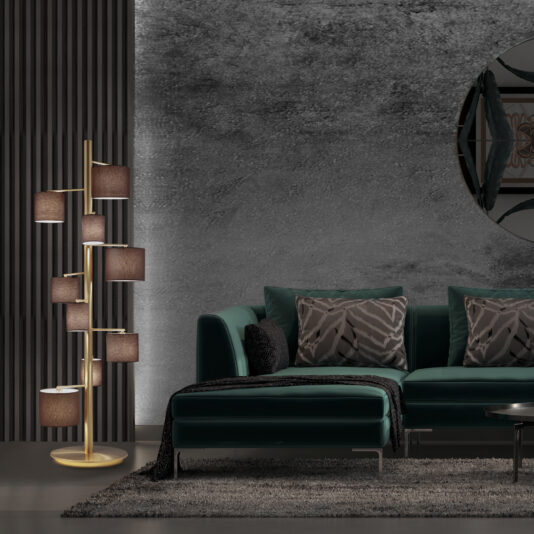 Modern Floor Lamp With Shades A modern living room featuring a dark green sectional sofa adorned with patterned cushions and a black throw blanket. The Modern Floor Lamp With Shades, showcasing unique, multi-tiered design and shades in varying browns, stands beside the sofa. The room's ambiance is further enhanced by dark textured and slatted walls, complemented by a round decorative mirror.