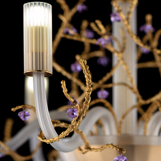 Close-up of the **Modern Wall Light With Swarovski Crystal Flowers**, adorned with gold twisting branches and purple gemstone accents. The wall light showcases sleek, white candle-like fixtures, highlighting the intricate design details against a dark background.