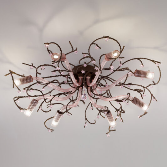 A decorative ceiling light fixture with an intricate, floral-inspired design features twisting branches capped with small pink glass flowers and Swarovski crystal accents that extend outward, holding cylindrical light bulbs that cast a soft, ambient light. The Pink Glass Branch Ceiling Light With Swarovski Crystal Flowers is mounted on a white ceiling.