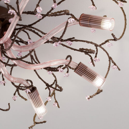 A close-up view of the Pink Glass Branch Ceiling Light With Swarovski Crystal Flowers shows its intricate design, featuring twisted metal branches adorned with small, pink crystal-like ornaments and several cylindrical light bulbs encased in ribbed glass coverings, arranged to resemble a blossoming tree.