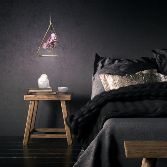 Rose Crystal Rock Pendant Light A modern bedroom with a dark aesthetic features a wooden side table next to the bed, holding a white statue, a cup, and books. Above the table hangs the Rose Crystal Rock Pendant Light with its geometric design and central rose crystal rock pendant. The bed is adorned with dark linens and decorative pillows.