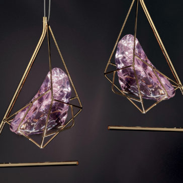 This image showcases two exquisitely crafted Rose Crystal Rock Pendant Lights, adorned with translucent purple glass birds and encased in geometric gold-colored wire frames. The dark background accentuates the intricate details and elegant craftsmanship of these stunning fixtures.