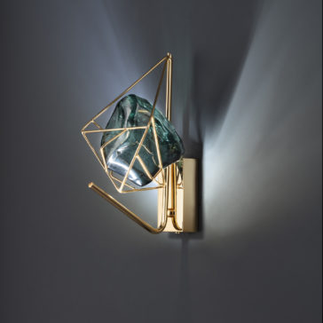 Viridian Green Crystal Rock Wall Light The Viridian Green Crystal Rock Wall Light features a modern gold geometric frame that encloses an irregularly-shaped, translucent viridian green glass piece. It emits soft light, creating decorative patterns on the grey wall, combining contemporary design with artful illumination.