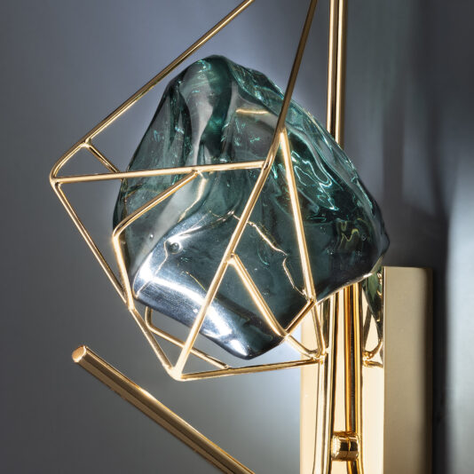 The Viridian Green Crystal Rock Wall Light boasts a contemporary and artistic design, featuring a large, irregularly shaped viridian green crystal rock encased in a geometric gold metal frame. This stunning piece blends natural and industrial elements seamlessly.